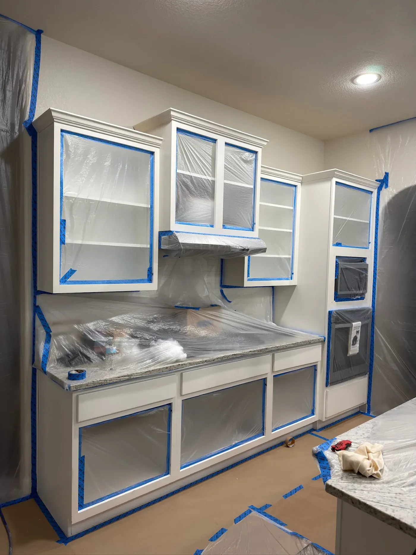 Kitchen cabinets fully masked with blue tape and plastic before spray painting, Austin TX