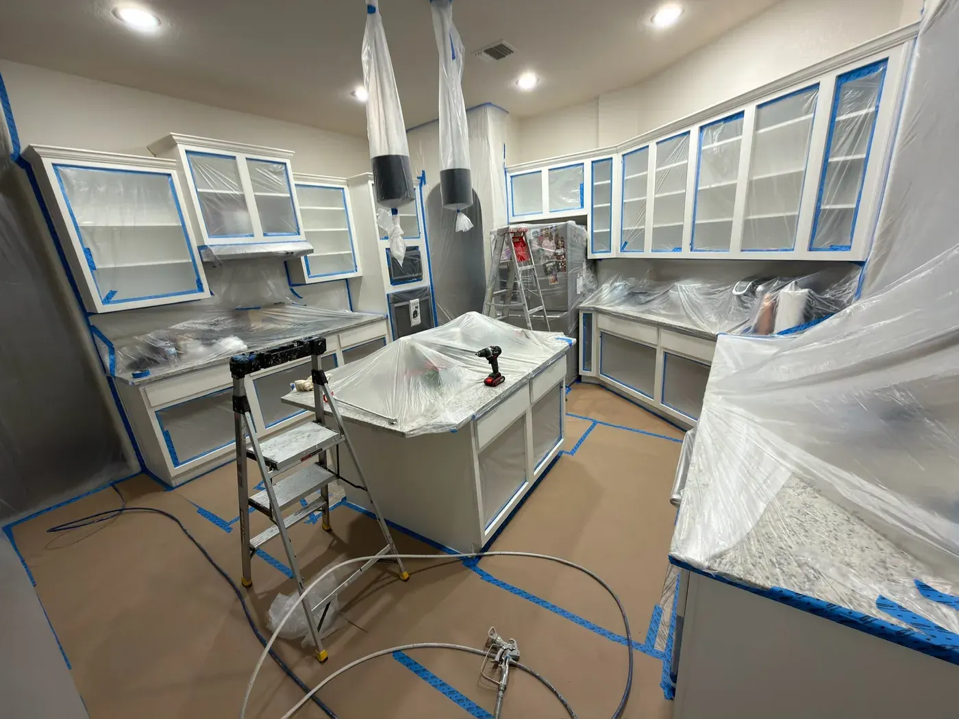 Kitchen during cabinet spray painting, full containment with plastic sheeting and airless sprayer, V&S Painting Austin